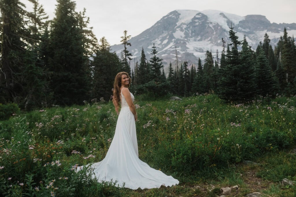 Bride stands in flower field at her Mt. Rainier elopement.