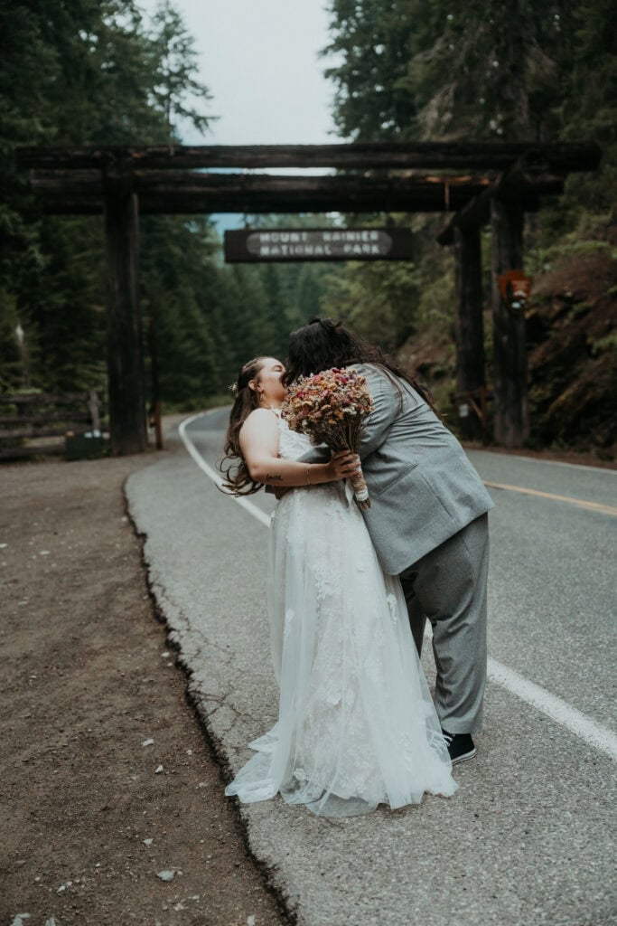 elopement couple kissing in front of mt rainier national park sign